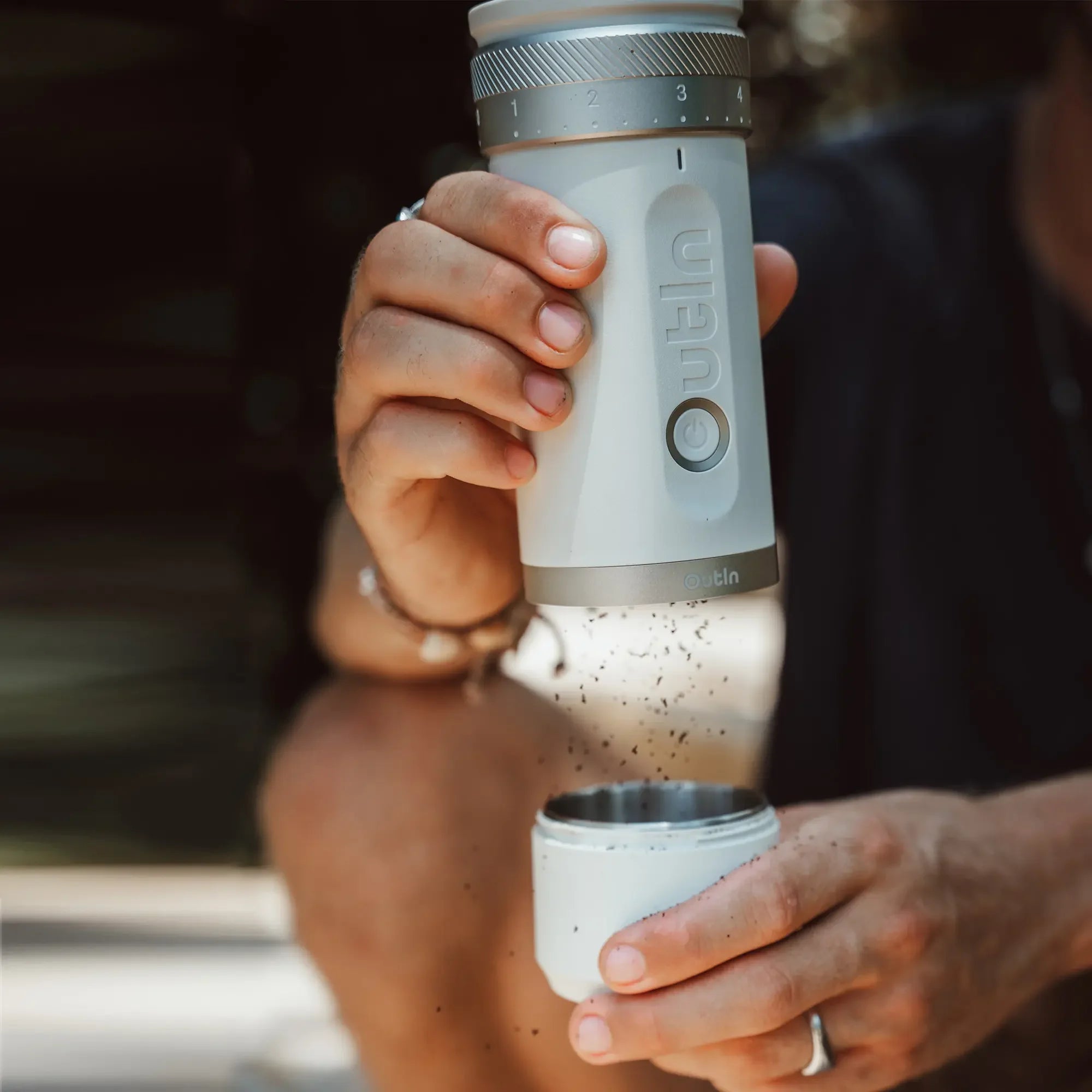 OutIn Fino portable coffee grinder in white dispensing fresh grounds into collection cup, showcasing compact design.