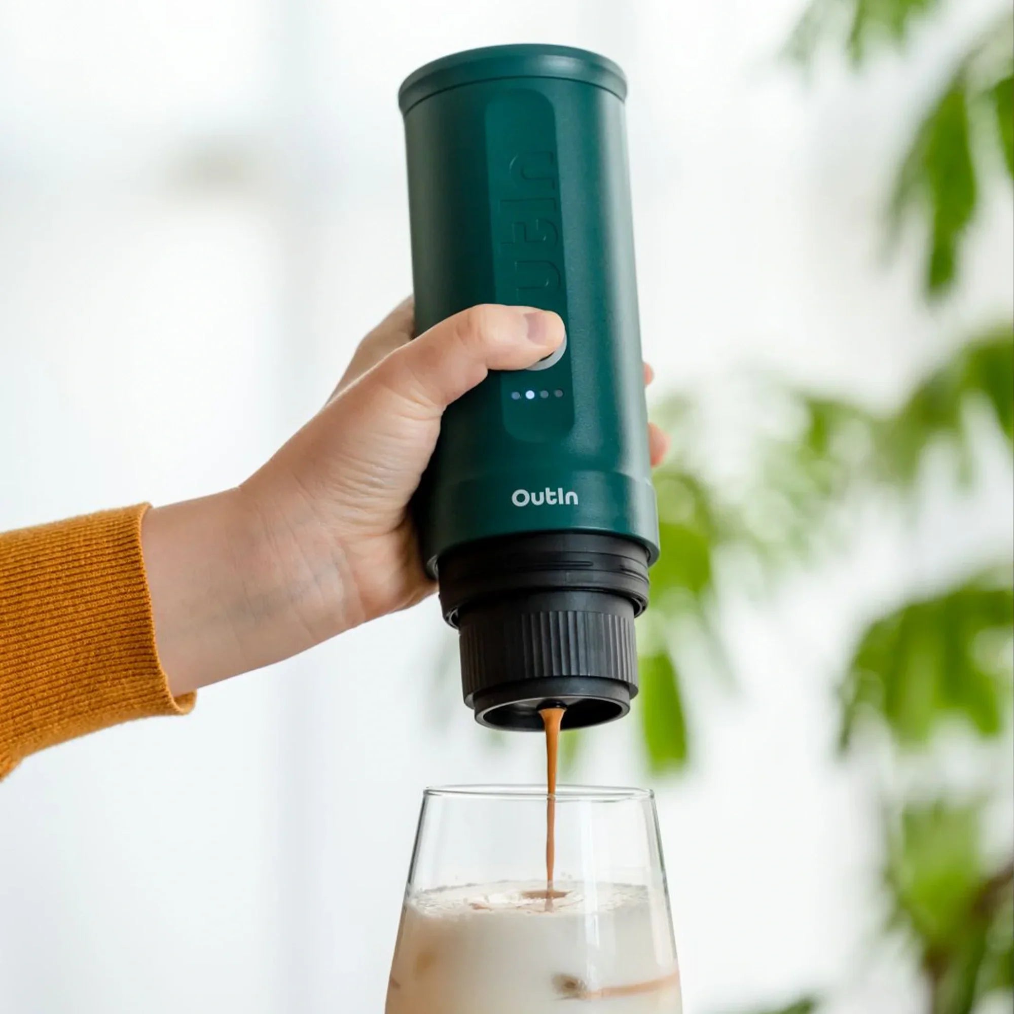 OutIn teal nano portable espresso machine brewing rich espresso into iced coffee in glass.