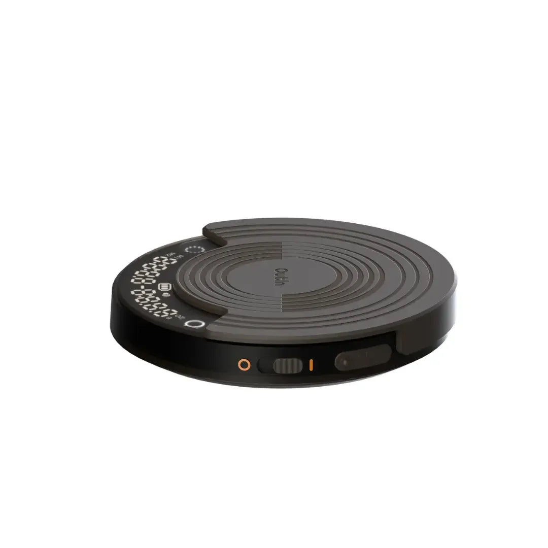 OutIn Claro coffee scale, round dark gray with concentric texture, digital display shows timer & weight, side power switch.