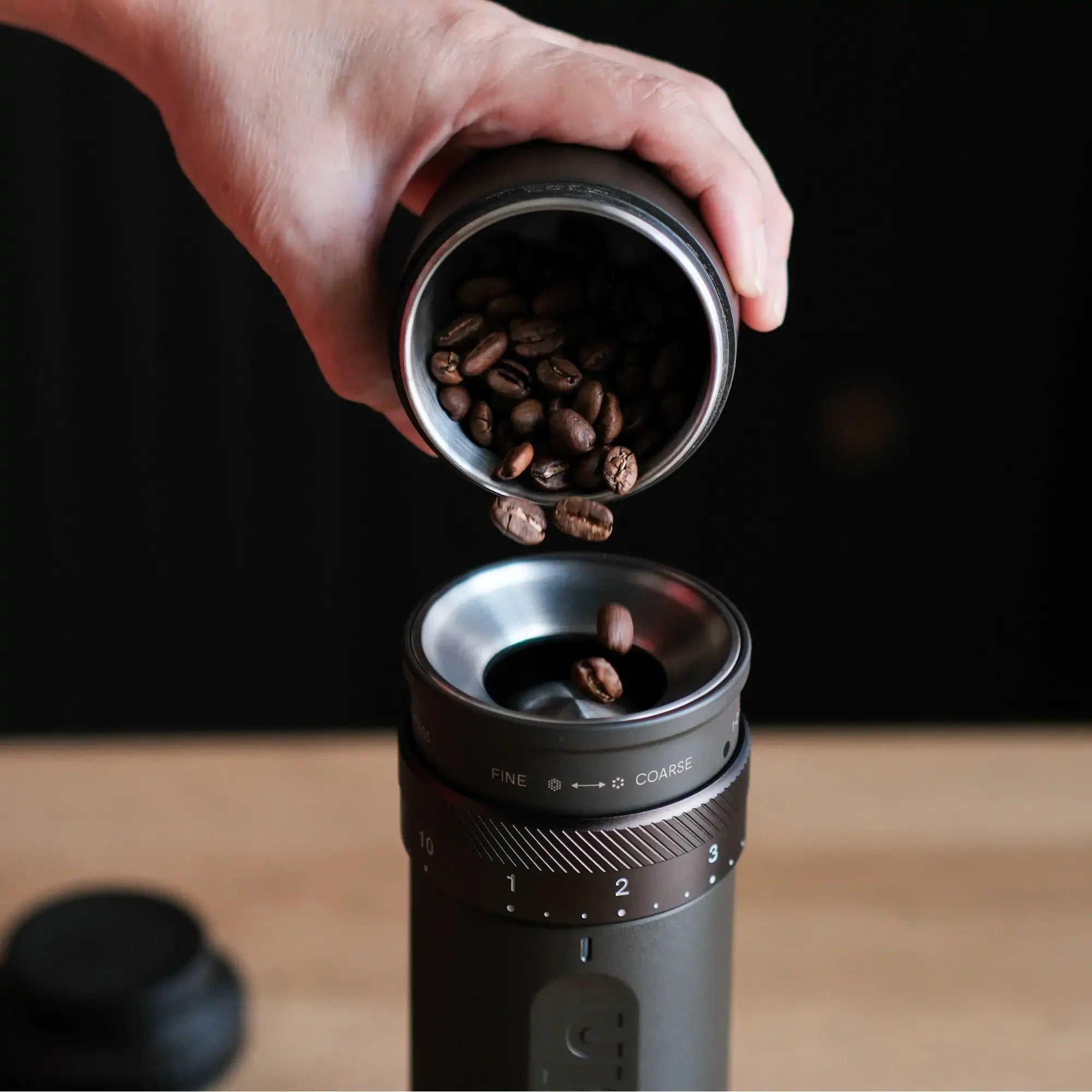 Grey OutIn Fino portable coffee grinder with hand adding coffee beans, showing grind settings.