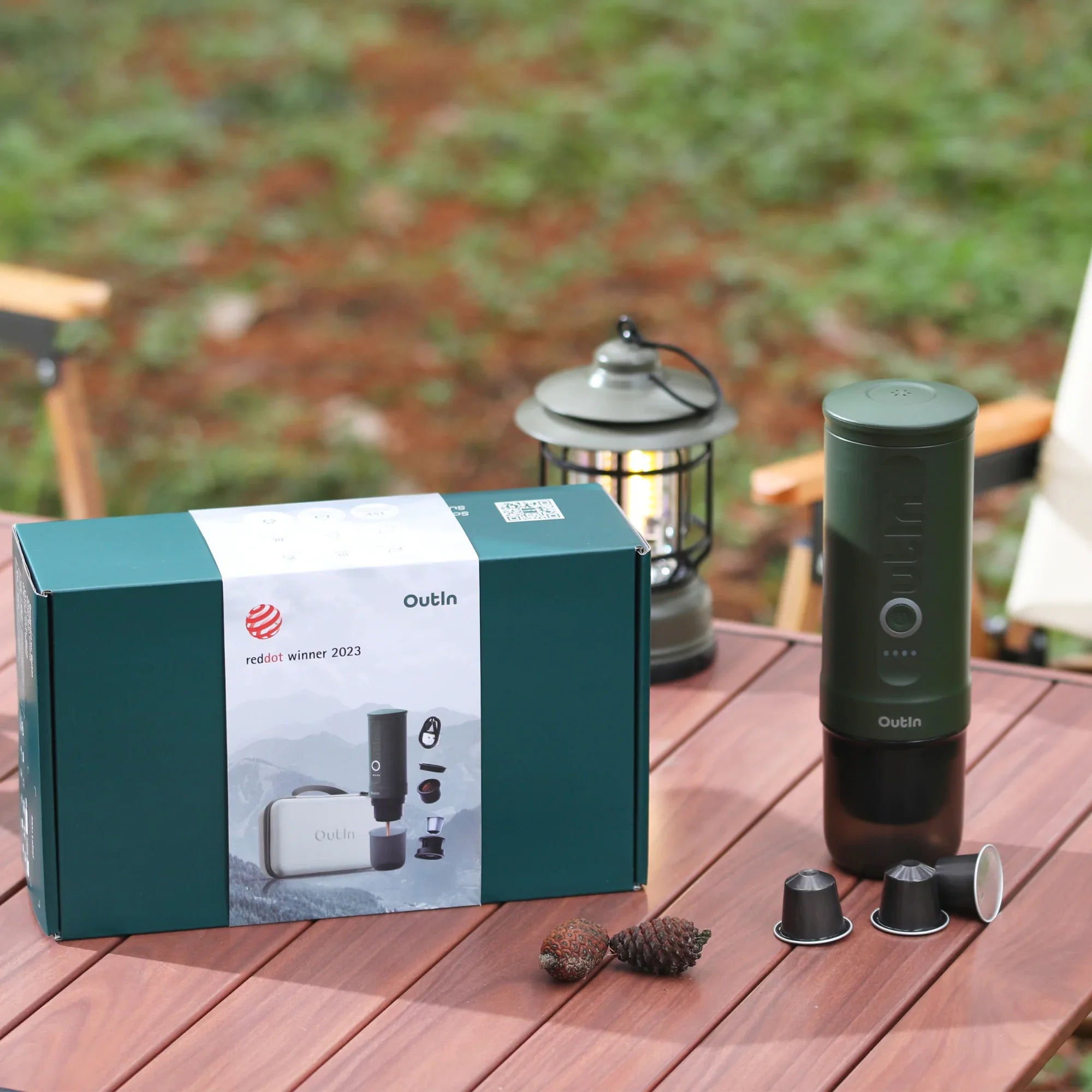 Forest green Traveler Espresso Gift Set with portable maker, packaging, protective case, pine cones, lantern on wood table.