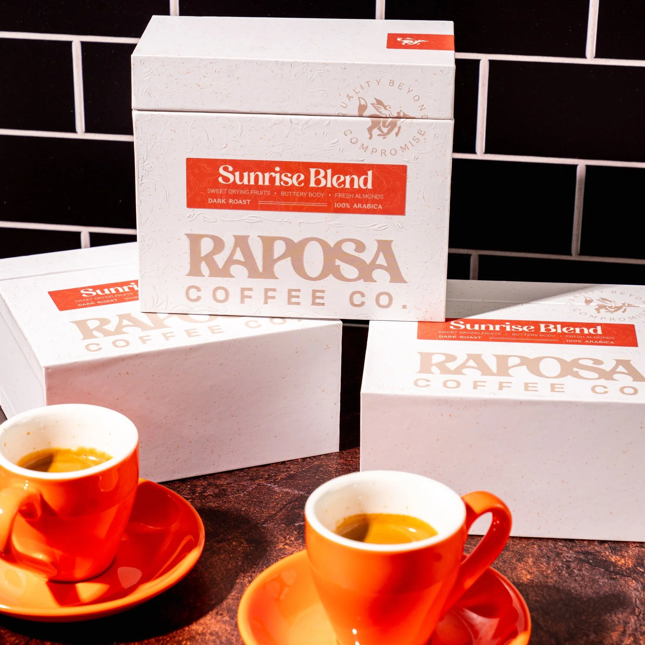 Raposa Coffee Co. Sunrise Blend dark roast specialty coffee bean boxes with two orange espresso cups of fresh coffee.