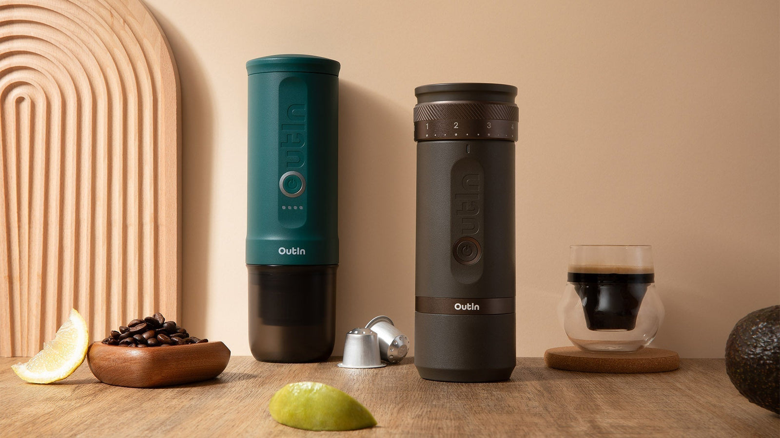 Two Outin portable espresso makers in white and dark brown, displayed with coffee capsules and beans