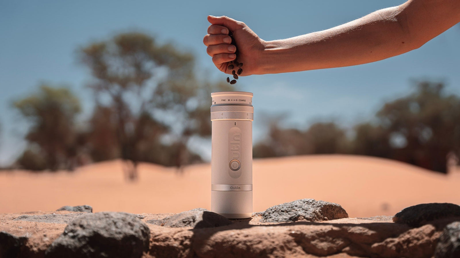 Adding coffee beans to Outin portable grinder for fresh espresso in outdoor desert adventure