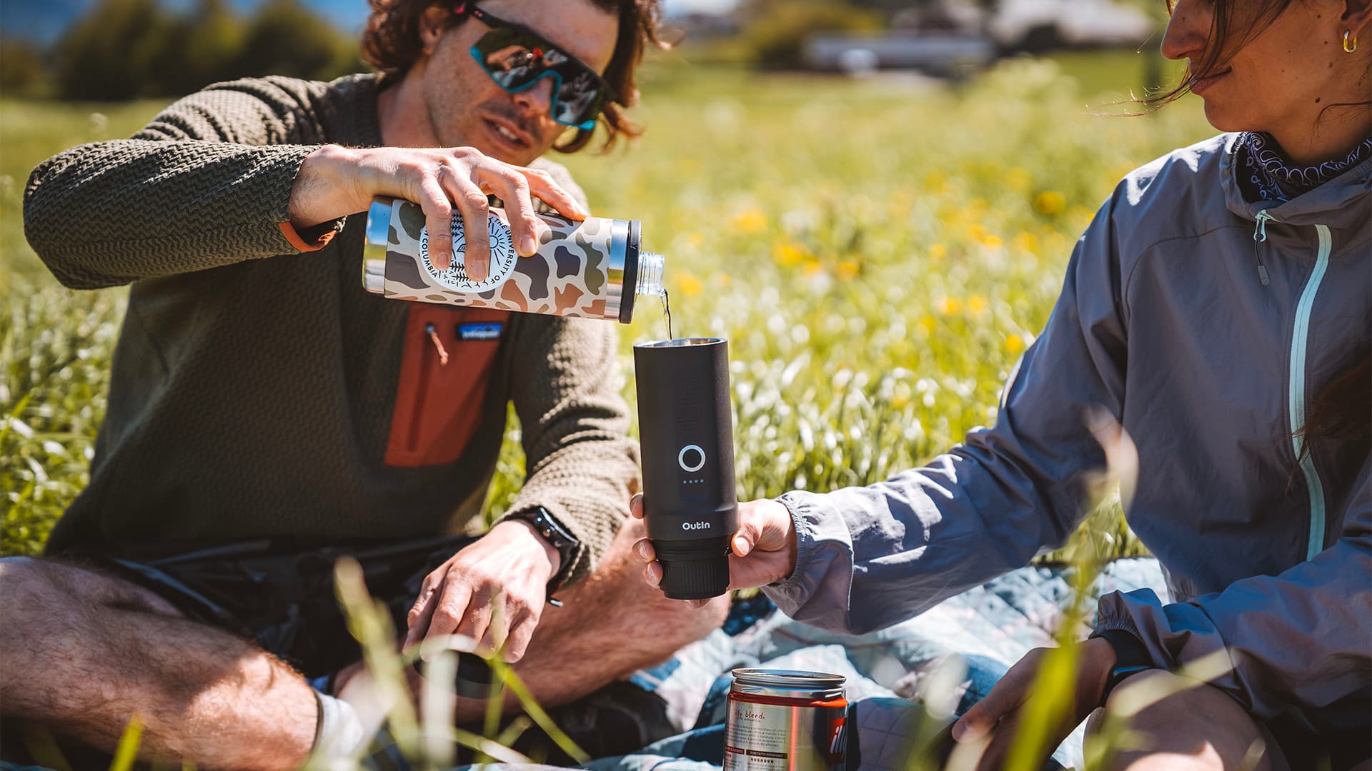 Two people enjoying a picnic outdoors with one pouring water into an OutIn portable espresso machine