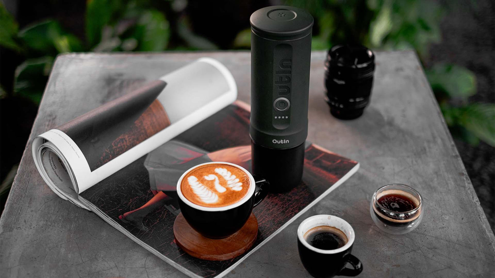 Outin portable espresso maker with logo next to a latte with latte art on a coffee table