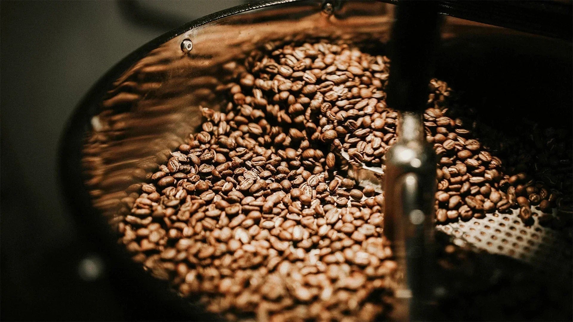 A close-up shot of light-to-medium roasted coffee beans tumbling inside the drum of a commercial coffee roasting machine