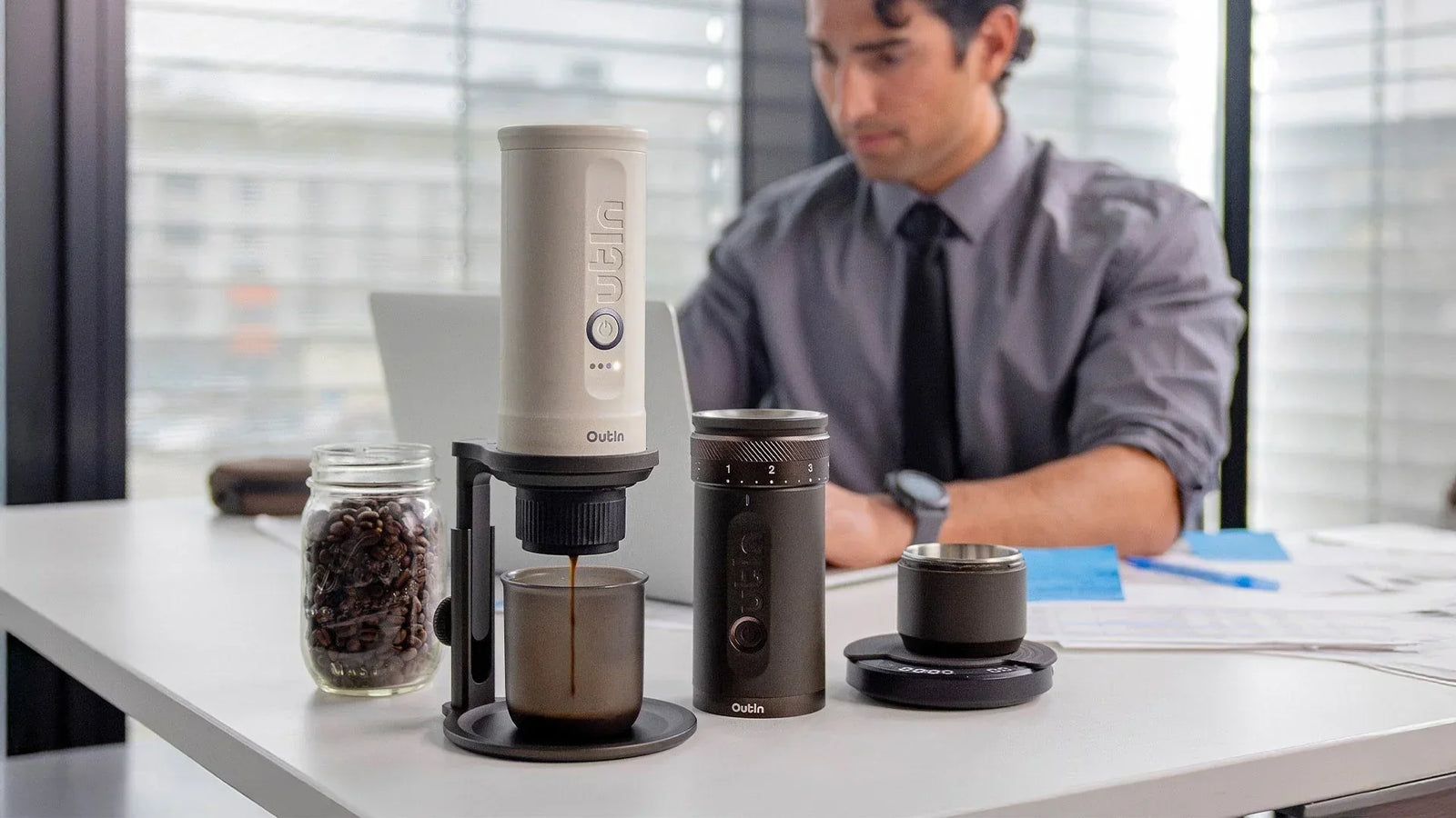 An office worker uses the Outin Fino Portable Electric Coffee Grinder and other Outin accessories to brew coffee at his desk