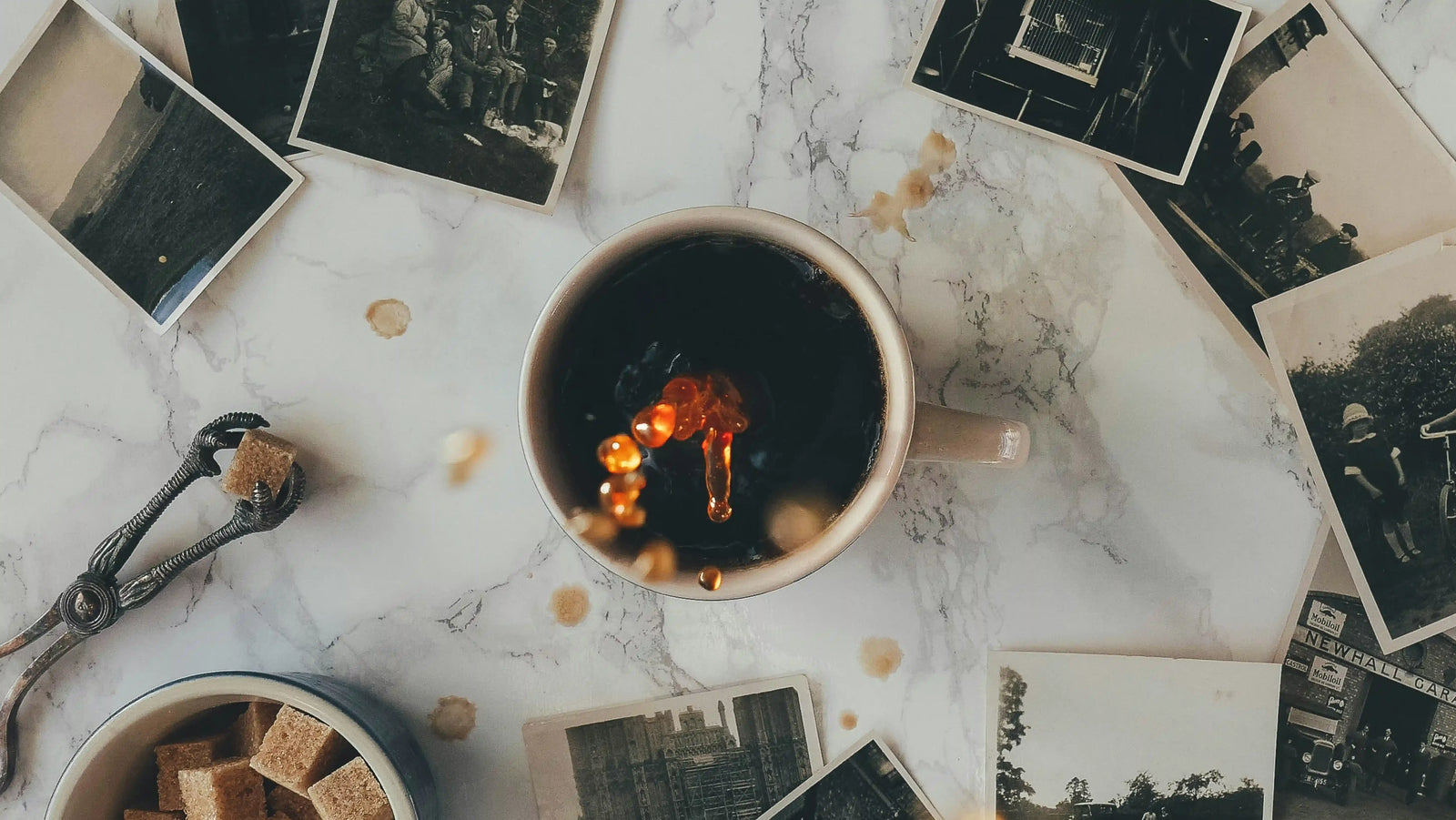 Cup of black coffee with vintage photographs scattered on marble surface, coffee droplets creating artistic reflections, nostalgic coffee moment