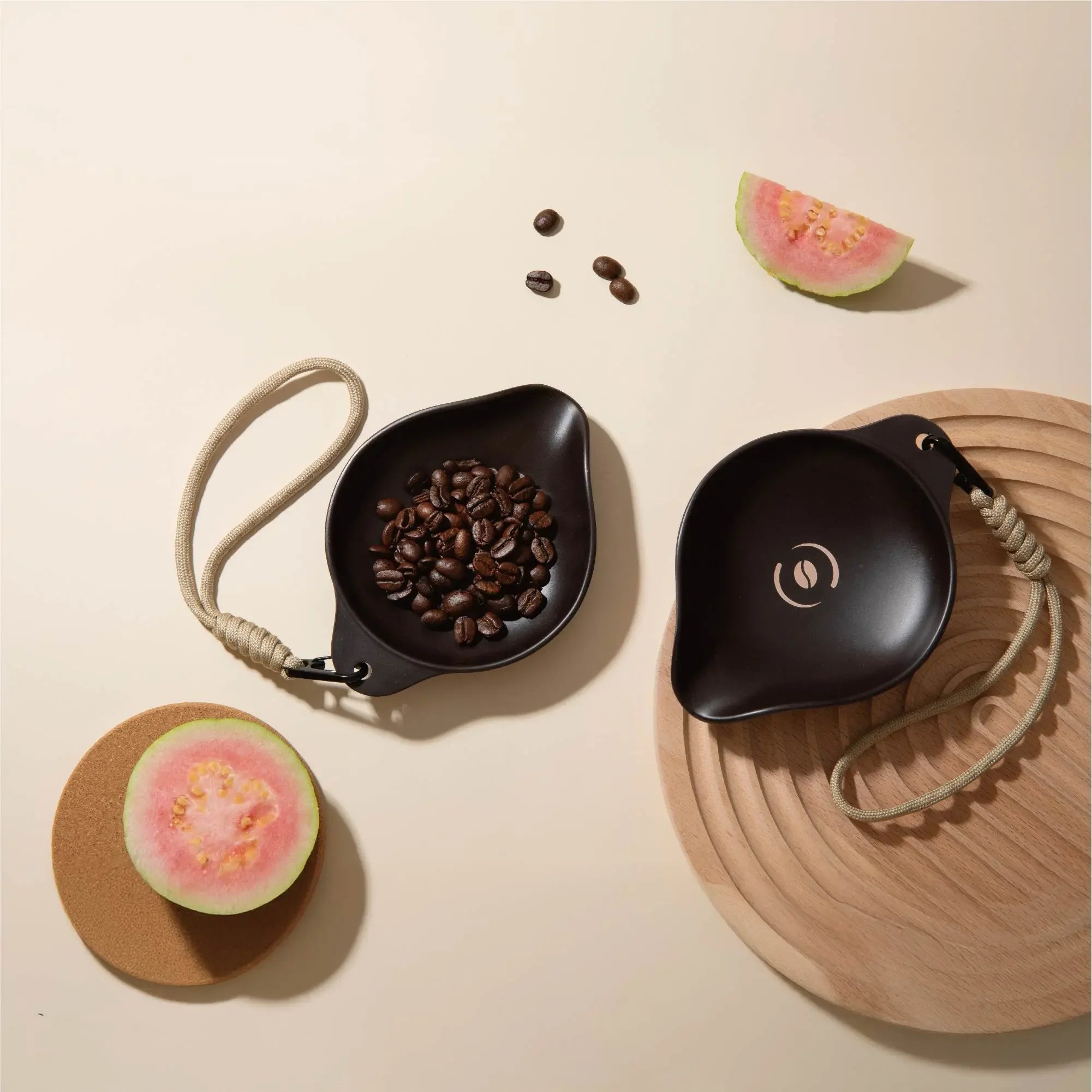 Two dark brown OutIn Rebrew bean trays, one with coffee beans, featuring braided lanyards for portability.