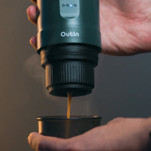 OutIn teal nano portable espresso machine brewing rich espresso with steam into a mug held by hands.