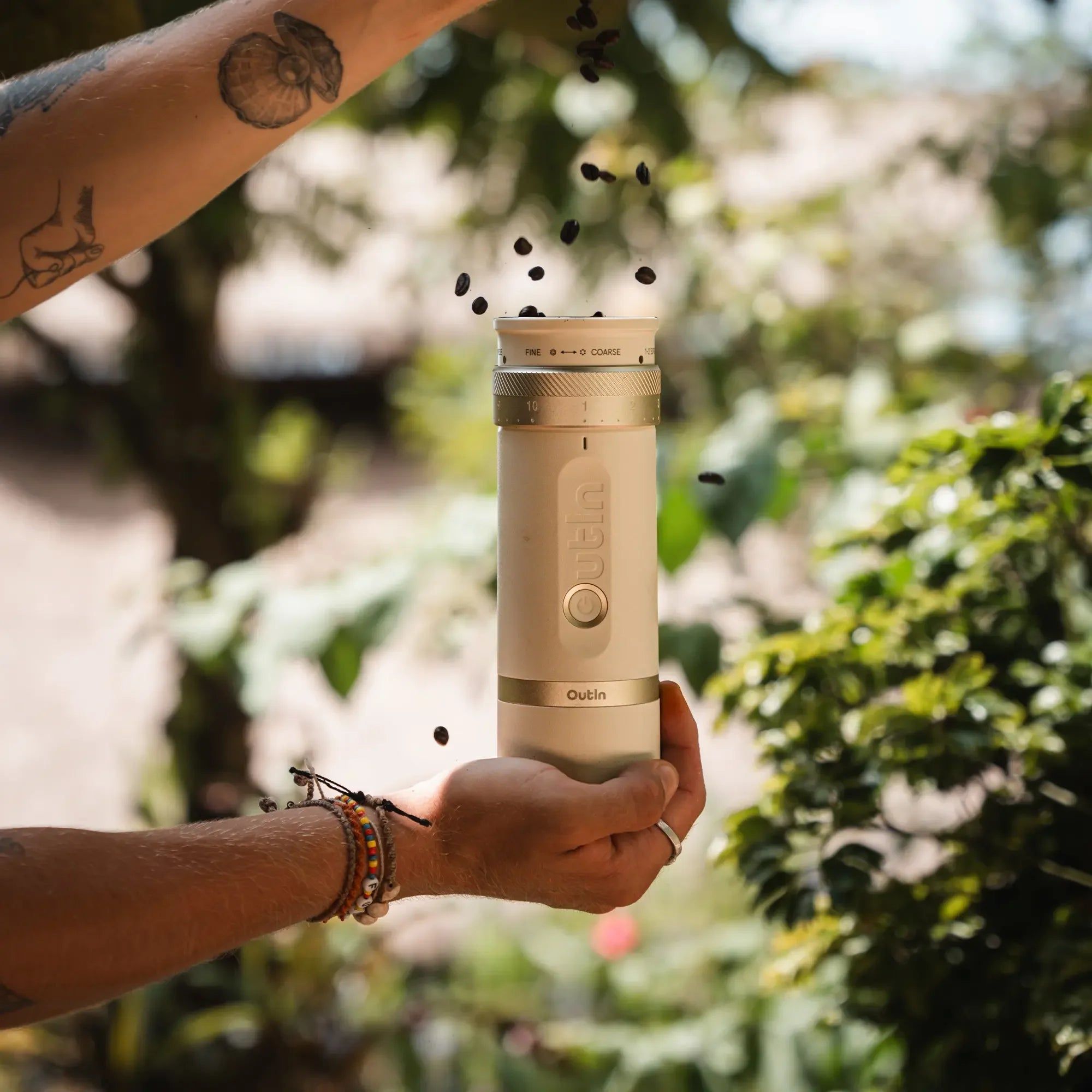Hands loading coffee beans into cream OutIn Fino portable electric coffee grinder, demonstrating grab-and-go convenience.