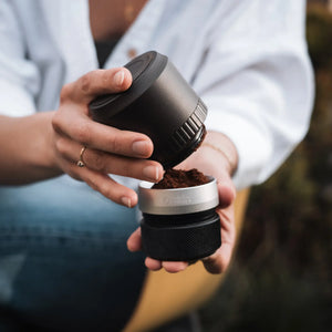 OutIn Fino portable coffee grinder dispensing fine grounds into detachable silver catch, showcasing sleek design.