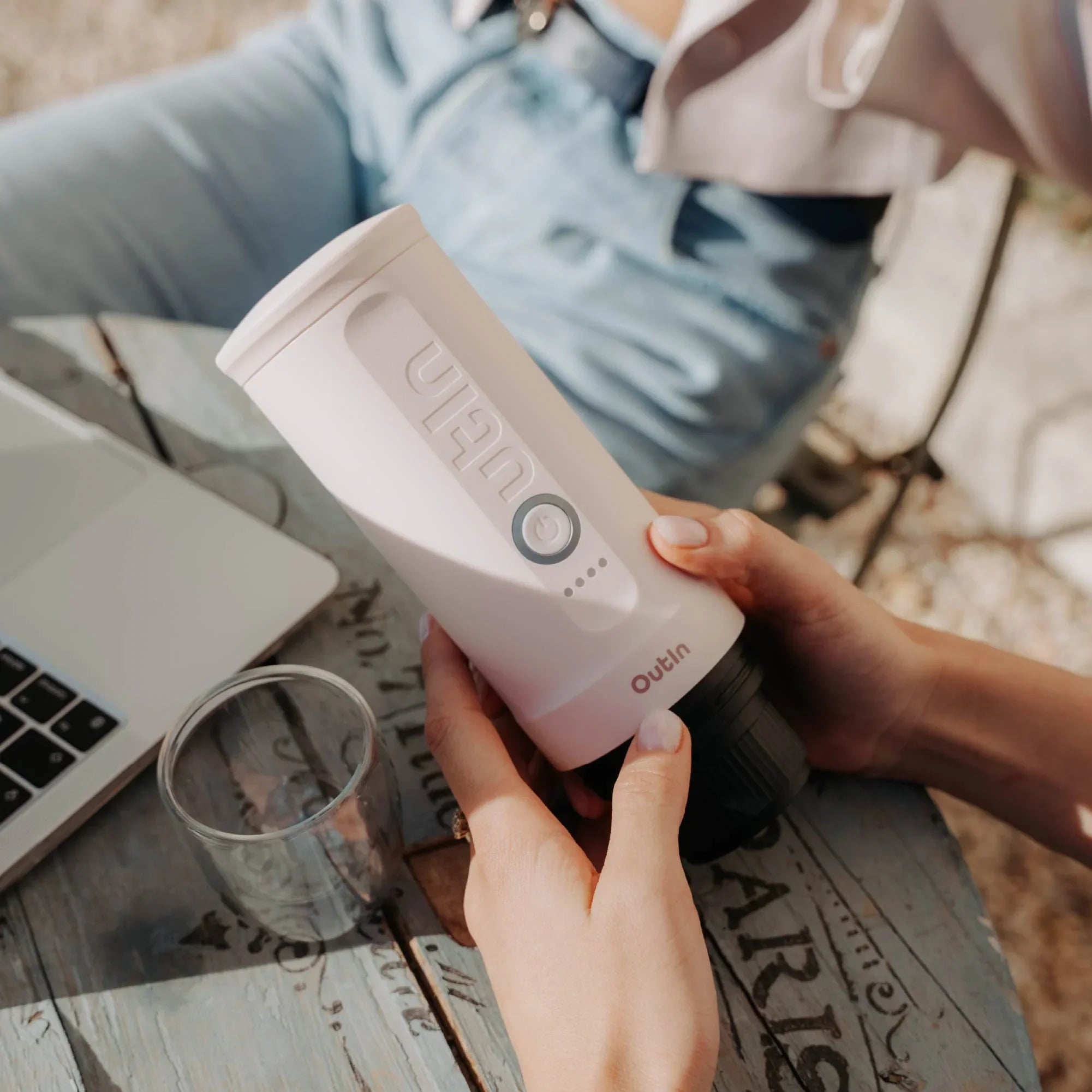 Rose Quartz Nano portable espresso machine in hand, with laptop and glass on table, showcasing portability.