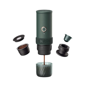 Dark green OutIn Mino portable espresso machine brewing coffee into a textured cup with grounds pod, lid, and capsule holder.