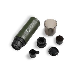 Forest green portable espresso maker with accessories including a cup, scoop, and coffee grounds on a white background.