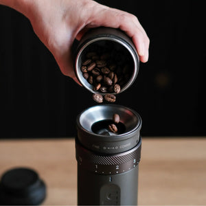 Grey OutIn Fino portable coffee grinder with hand adding coffee beans, showing grind settings.