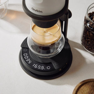 OutIn Claro coffee scale in dark gray, displaying 00:39 and 168.8g during espresso brewing. Coffee beans jar nearby.