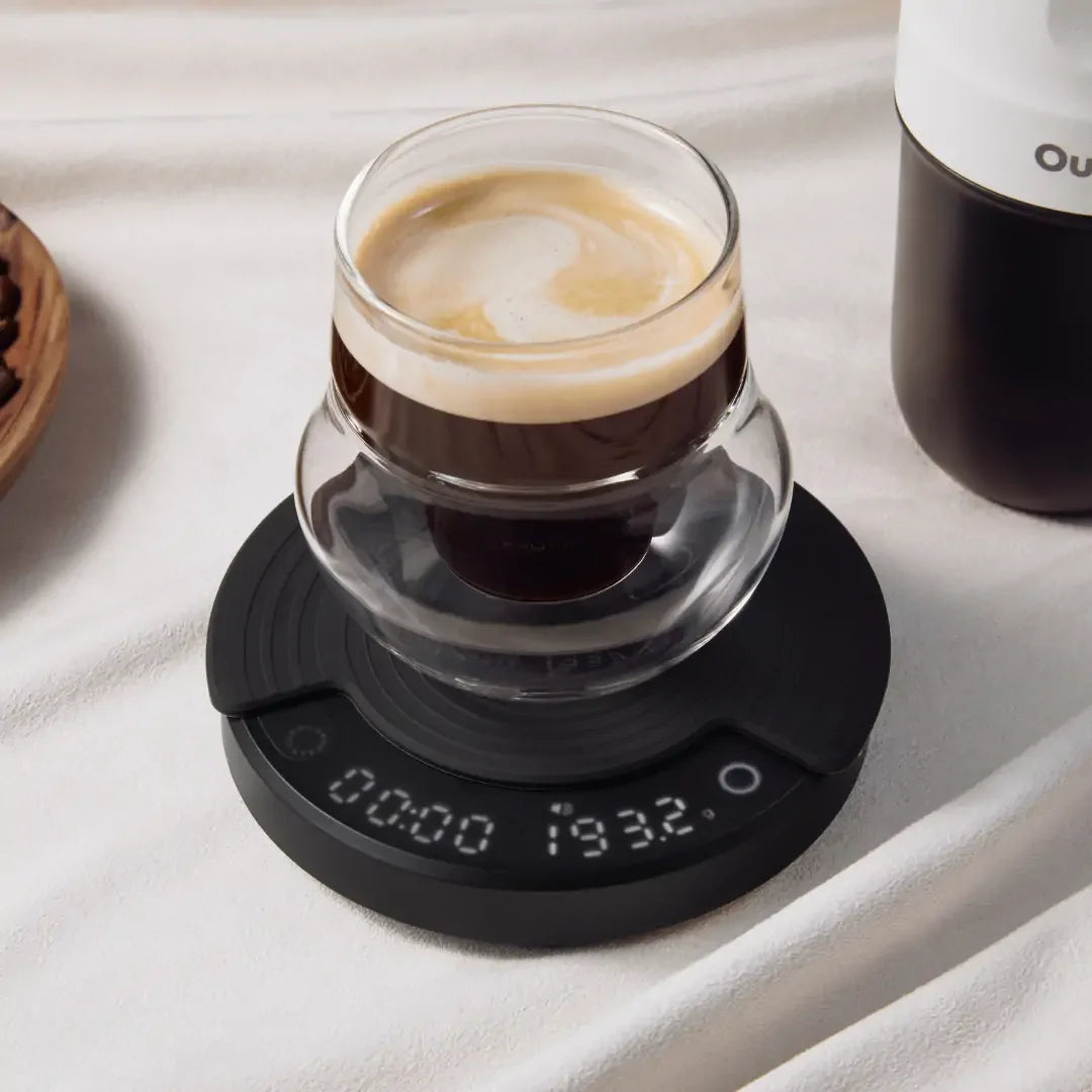 OutIn Claro black coffee scale weighing espresso. Display shows 00:00 193.2g. Coffee beans in background.
