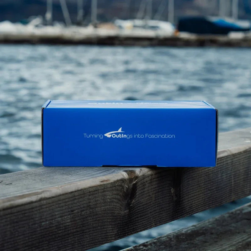 Ocean blue Nano portable espresso machine packaging with slogan "Turning OutIngs into Fascination" on a dock by the water.