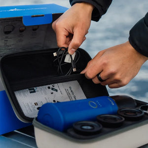 Person packing ocean blue Nano portable espresso machine and accessories into travel case with USB charger.