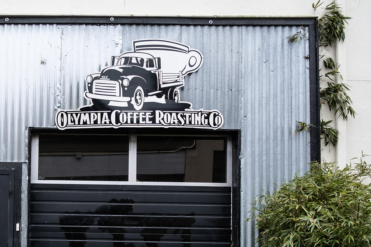 Olympia Coffee Roasting Co. vintage truck logo on corrugated metal wall, showcasing brand identity.