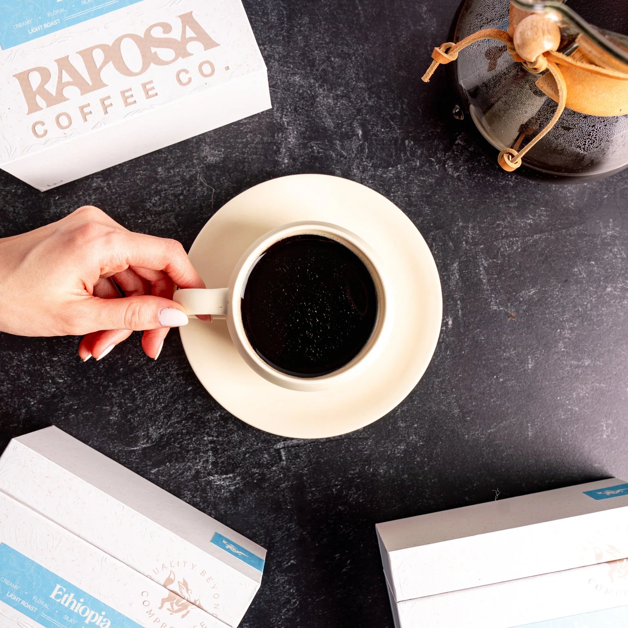 Raposa Coffee Ethiopia Light Roast box with creamy ceramic mug of coffee and Chemex brewer.