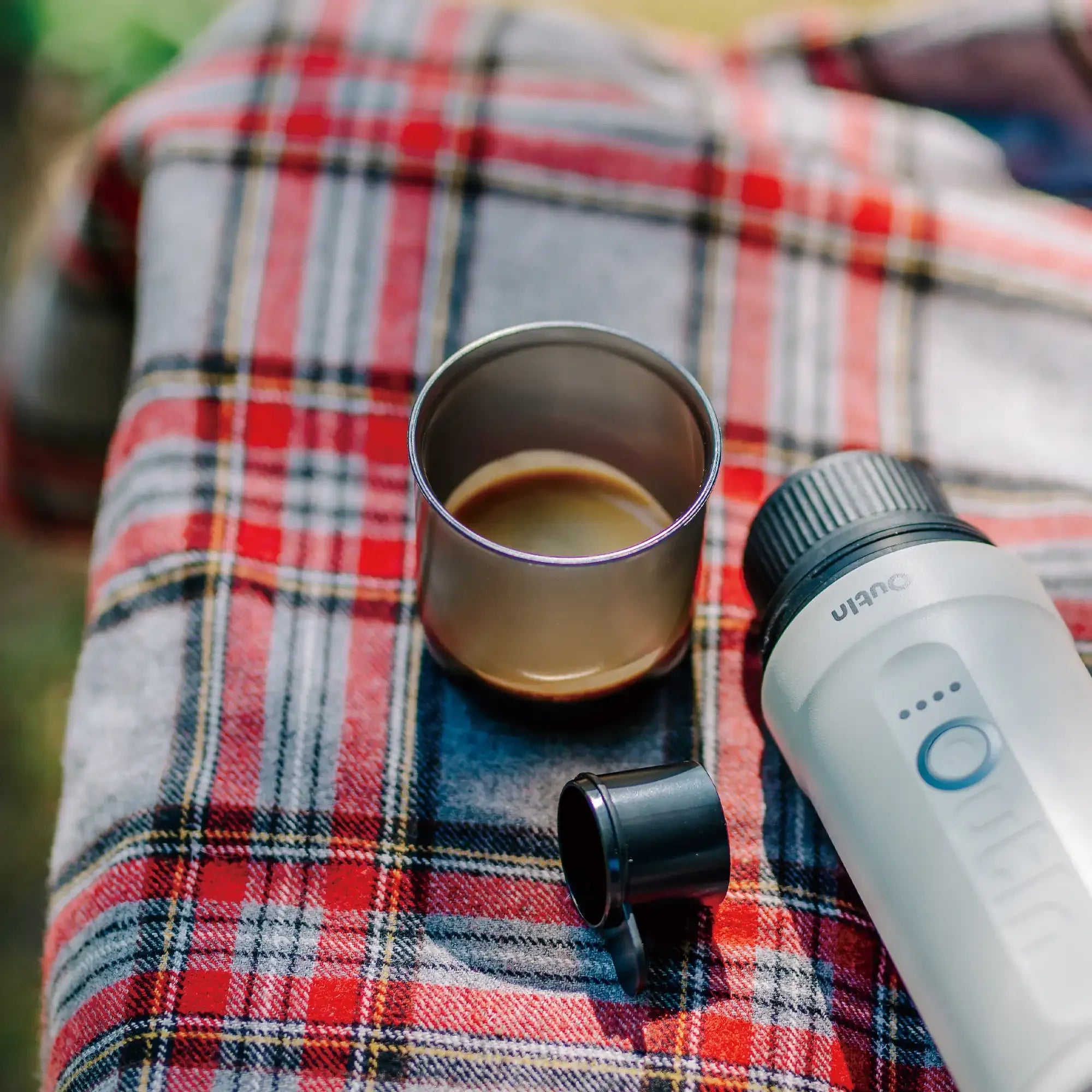 Nano Portable Espresso Machine Cup with espresso on plaid fabric next to OutIn portable machine for outdoor use.
