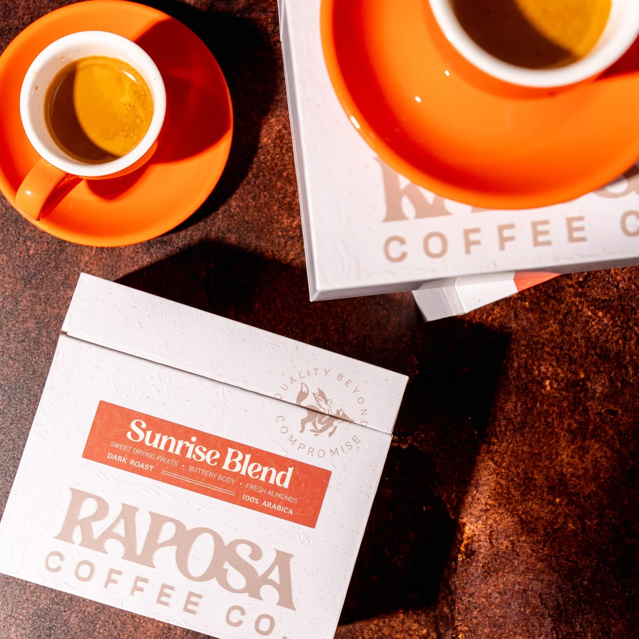 Raposa Coffee Co. Sunrise Blend dark roast beans, espresso cups on orange saucers. Notes: sweet fruit, buttery body, almonds.