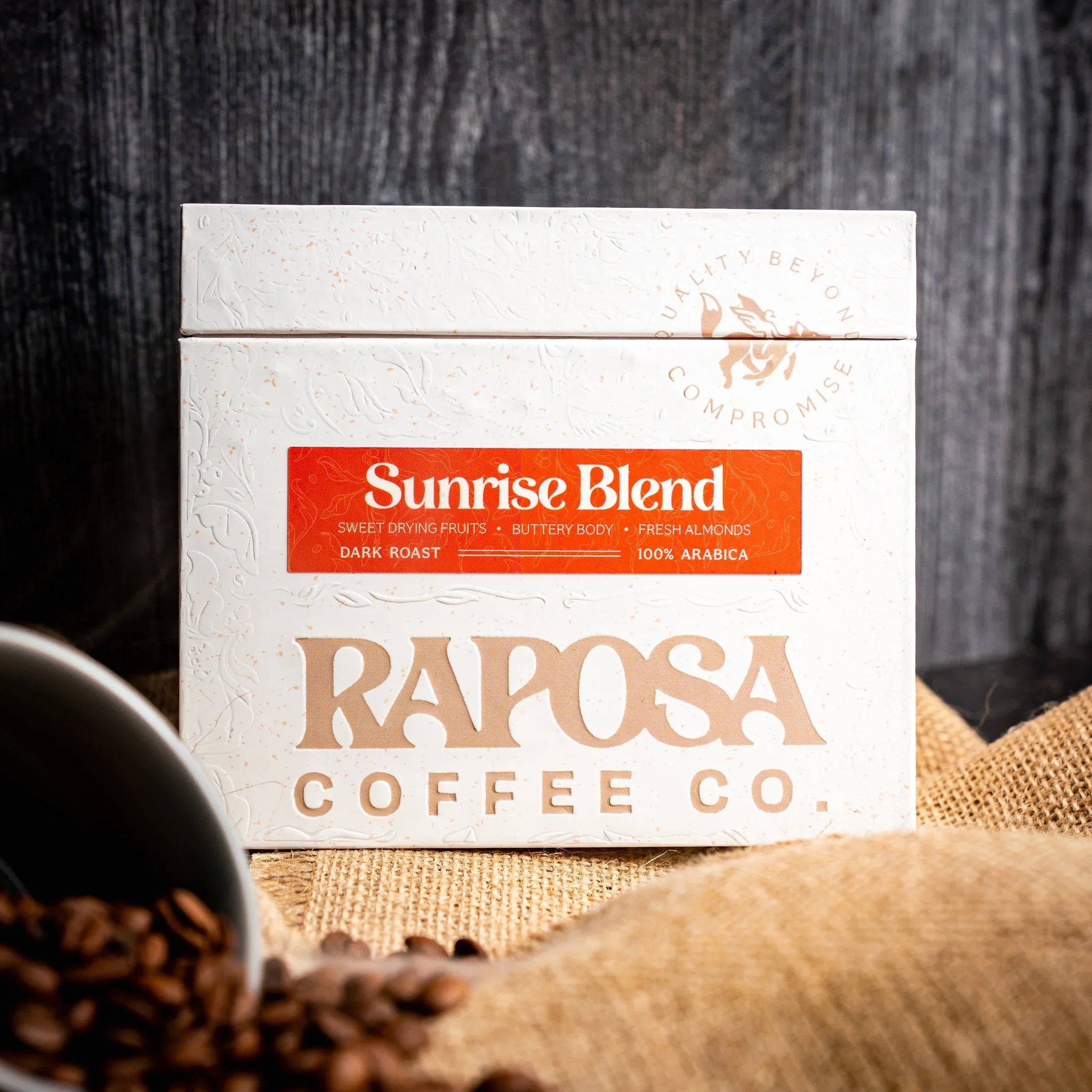Raposa Coffee Co Sunrise Blend dark roast whole coffee beans. White box, orange label. Notes: drying fruits, buttery, almonds.