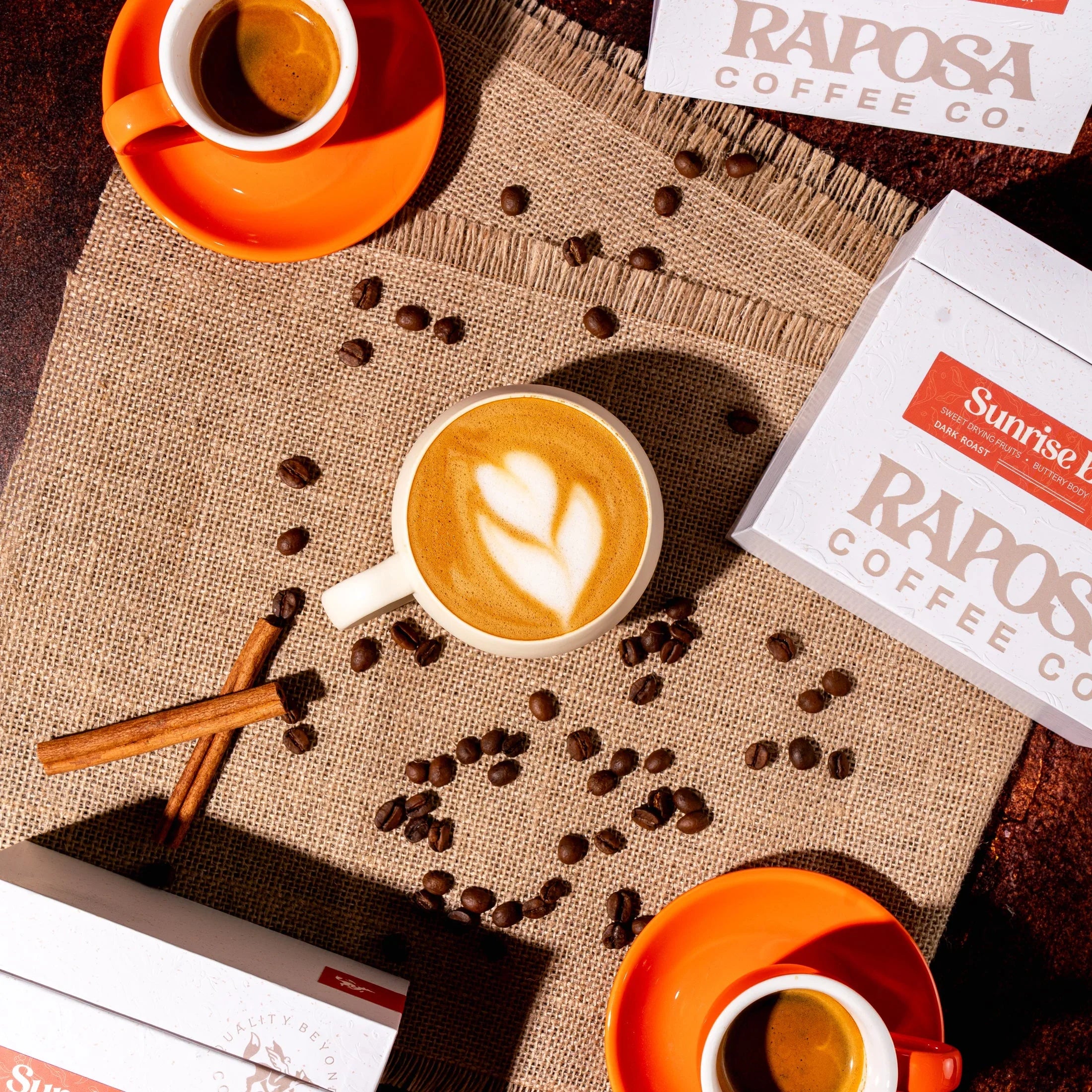 Raposa Coffee Co. Sunrise Blend dark roast coffee: latte art, espresso cups, beans, cinnamon, boxes on burlap.