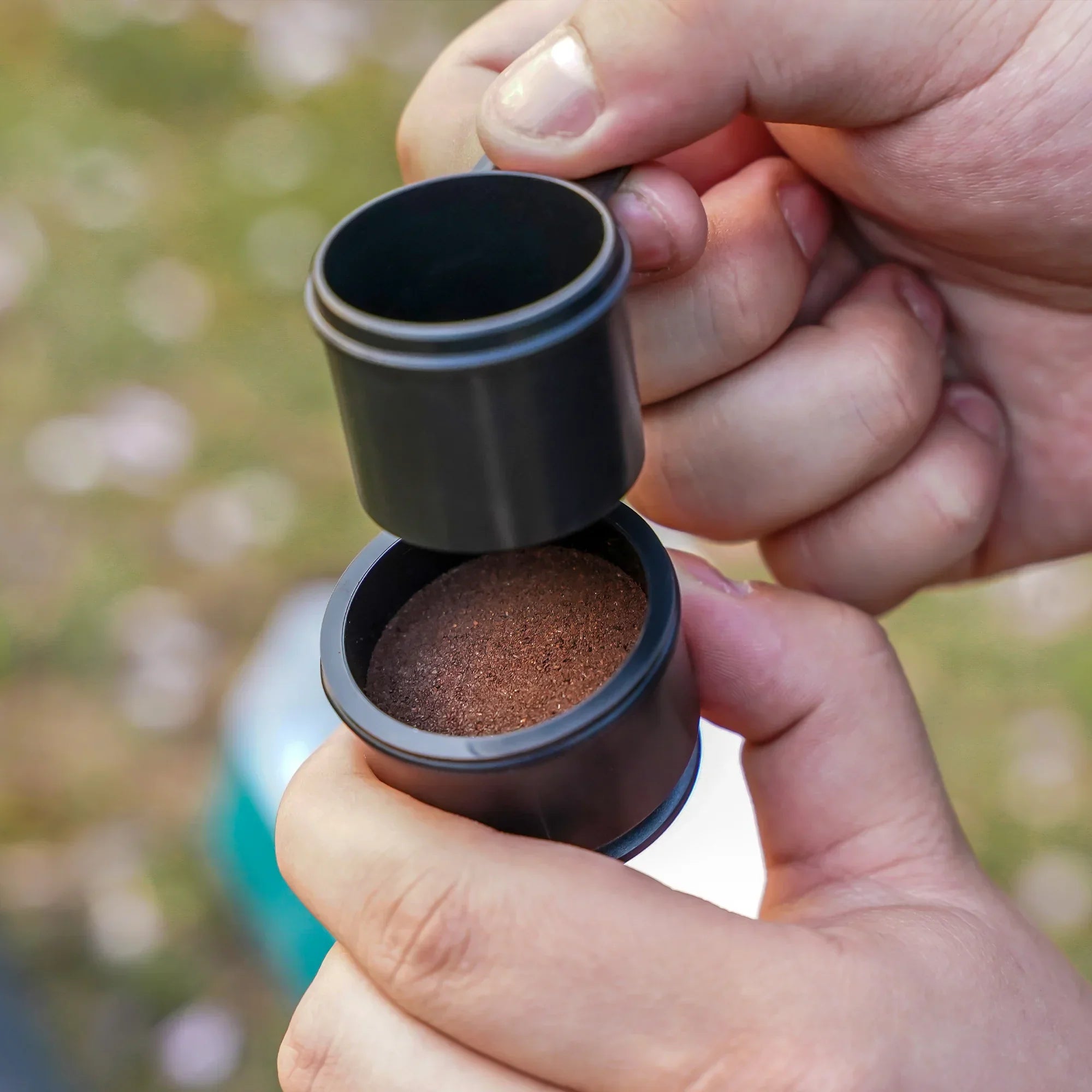 Hands using OutIn Nano espresso machine ground coffee filter basket with ground coffee and spoon for tamping. Product usage.
